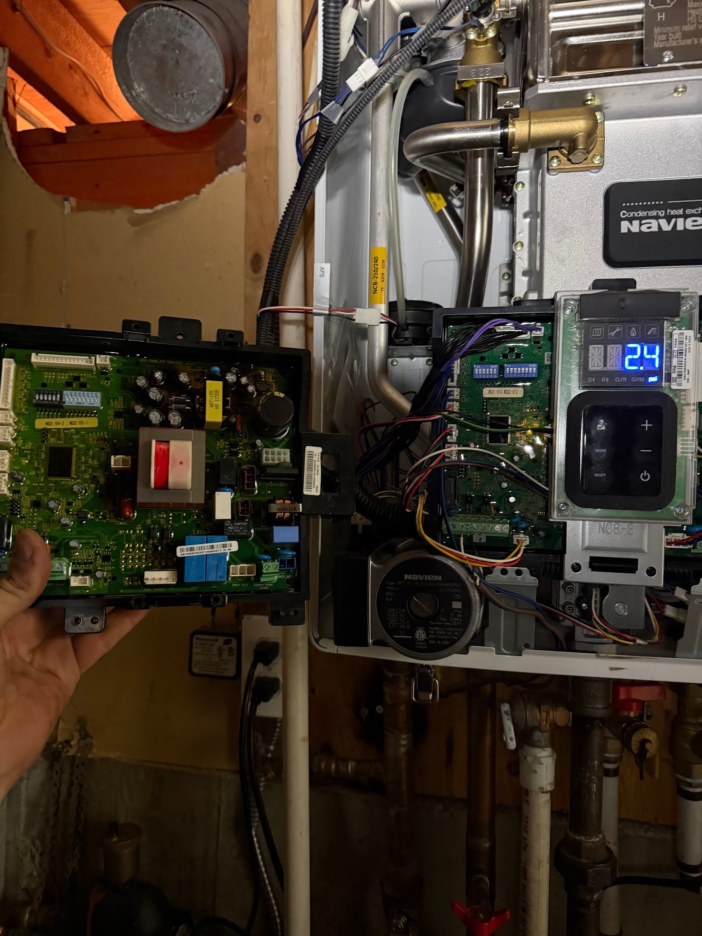 Control-board identification during boiler parts assessment Open Navien appliance with visible controls and a separate circuit board held beside it