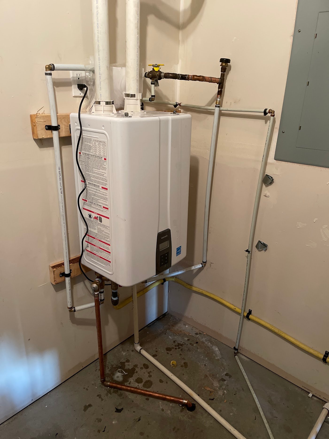 Wall-mounted appliance with twin white vent pipes, connected pipework and an electrical lead