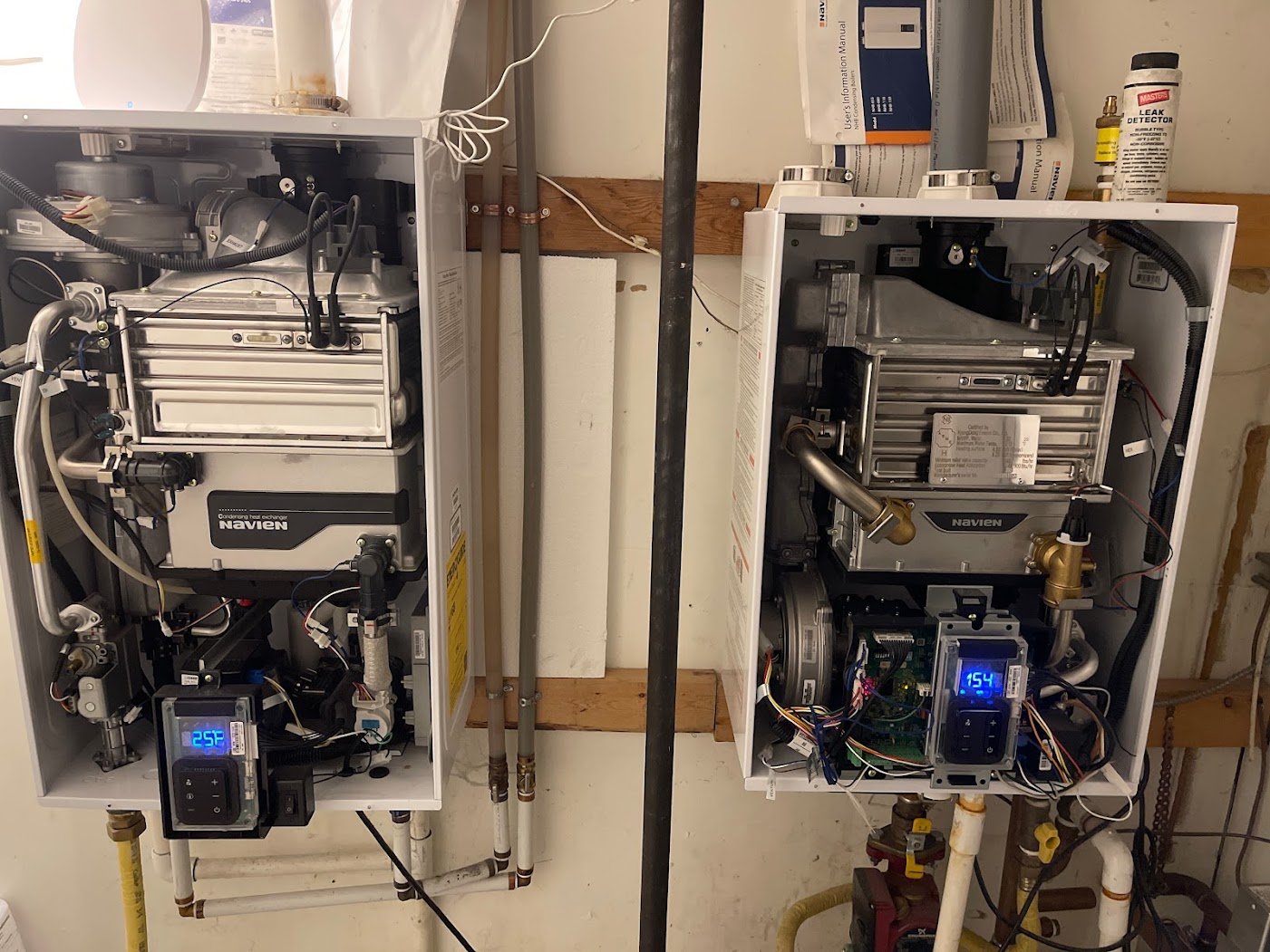 Two wall-mounted Navien appliances with front covers removed, visible heat exchangers, controls and connected pipework